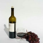 A sophisticated still life featuring red wine, a wine bottle, and fresh grapes on a white background.